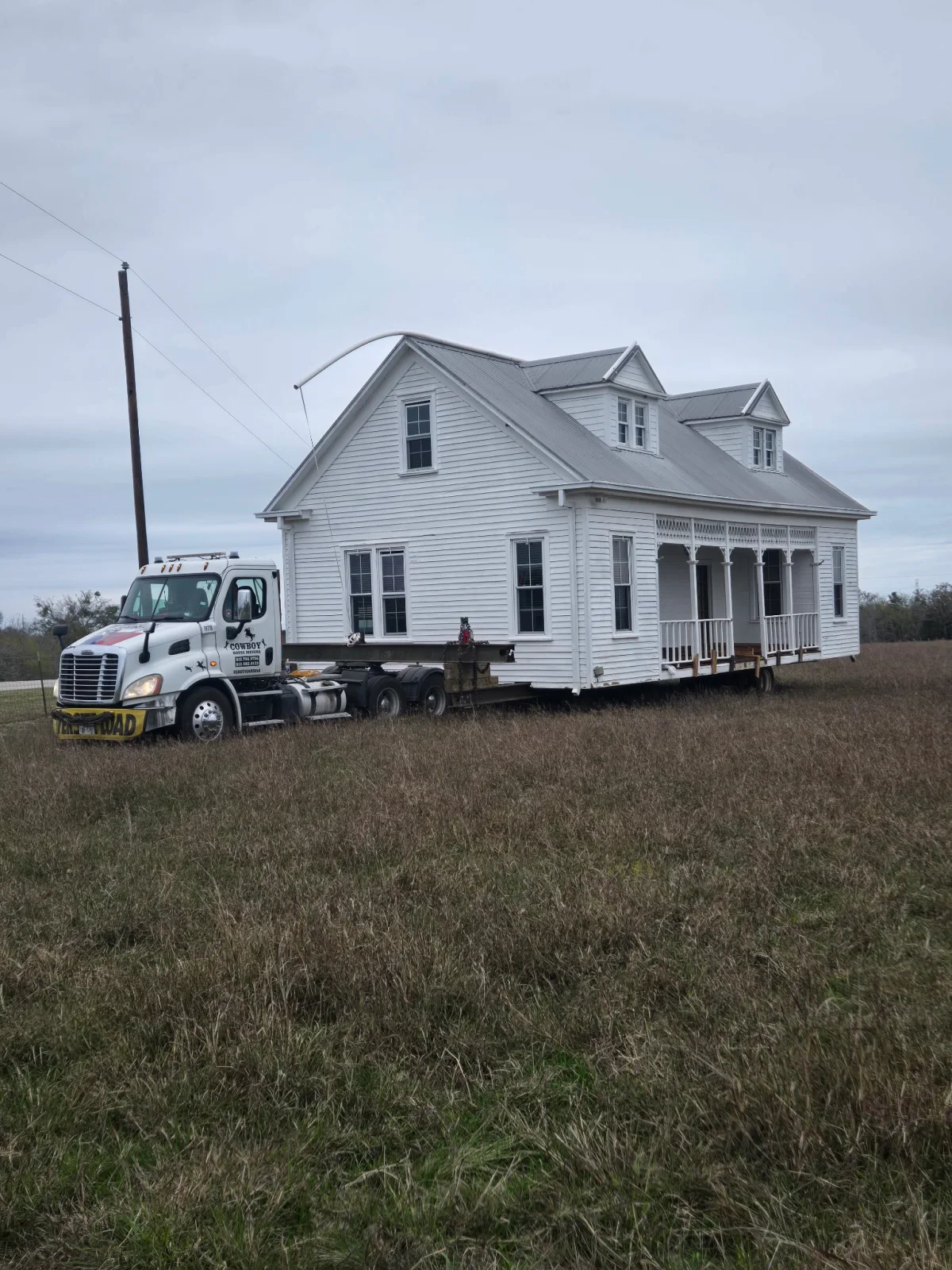 Cowboy House Movers transporting a white pier-and-beam house in Texas